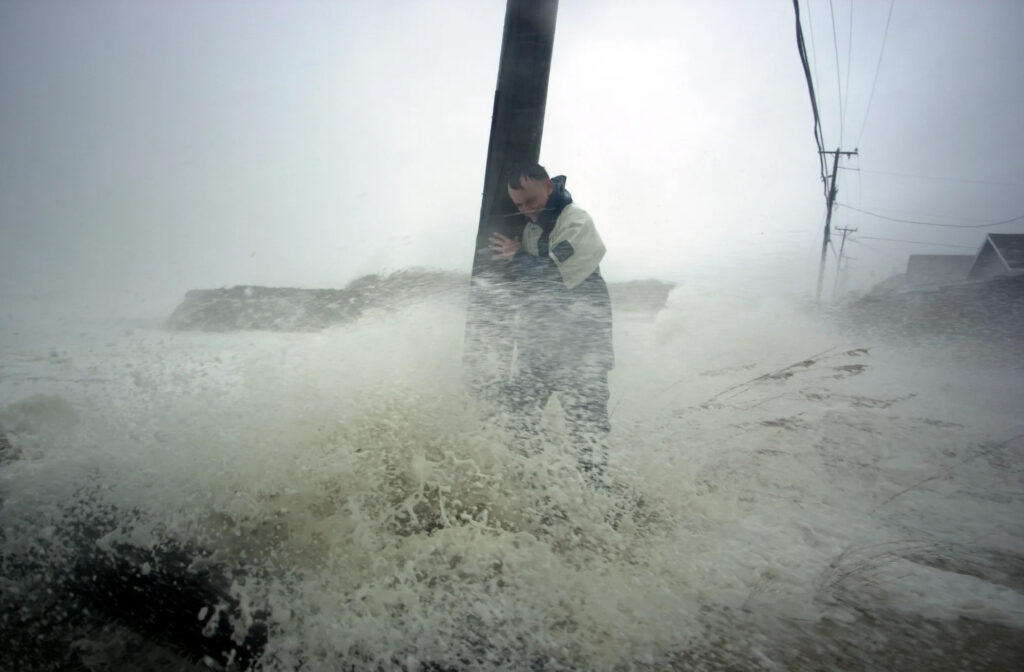 A photo of a man holding onto a telephone pole as waves crash around him during Hurricane Isabel